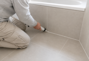 Handwerker erneuert Fugen im Badezimmer mit einer Kartuschenpistole.